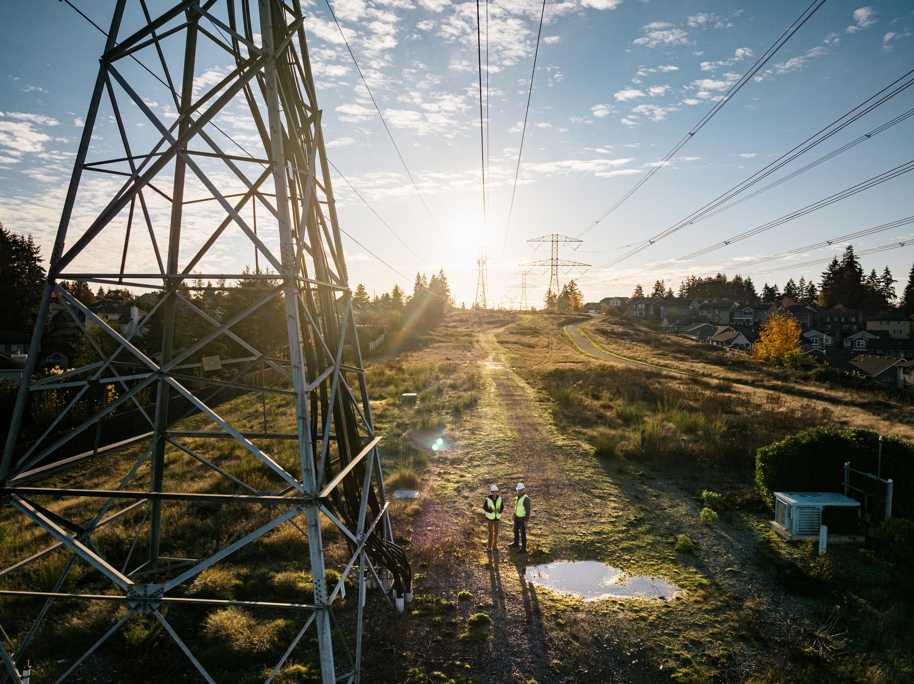 Transmission lines at sunset beside homes, energy infrastructure meeting community.